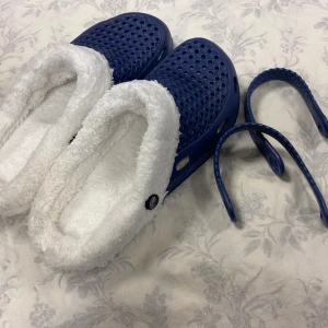 Blå tofflor med vit pälsfoder - Mysiga blå tofflor med avtagbara remmar och vit pälsfoder. Perfekta för kalla dagar hemma. Sulan är robust och ger bra grepp.           Storlek kvar 40,41 42 .                                 Tjocka fleece inuti, rekommenderar att välja 2 Stlk större än som är i vanlig, till exempel storlek 41 passar som är Stlk 39 i vanligt storlek 
