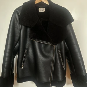 Svart skinnjacka från Twist & Tango - Säljer en snygg svart skinnjacka från Twist & Tango. Jackan har en mjuk, pälsliknande insida och en cool krage. Den har dragkedja och två fickor med dragkedjor. Perfekt för höst och vinter!