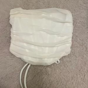 Vit tubtopp med snörning - Snygg vit tubtopp med snörning bak för en justerbar passform. Toppen har en rynkad design som ger en cool textur och stil. Perfekt för sommarens fester eller en dag på stan. Enkel att matcha med både jeans och kjol! Mesh matrial perfekt för utekväll eller nyår