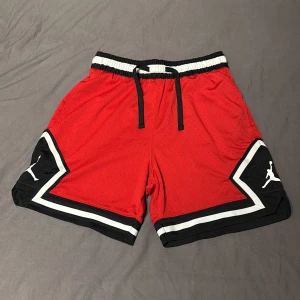 Röda jordan shorts - Säljer ett par röda jordan shorts i storlek M. De har en elastisk midja och svarta och vita detaljer på sidorna. Perfekta för träning eller bara hänga runt i. 