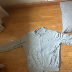 Grå tröja från Polo Ralph Lauren - Säljer en stilren grå tröja från Polo Ralph Lauren. Den har en dragkedja framtill och långa ärmar L men passar M. Perfekt för en avslappnad stil och passar bra till både vardag . Tröjan är i mycket bra skick och redo för en ny ägare! Priset är diskuterbart.