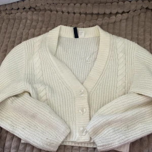 Vit stickad kofta från H&M - Superfin vit stickad kofta från H&M i storlek XS. Den har en mysig kabelstickad design med knappar framtill och en v-ringad hals. Perfekt för kyliga dagar och att mysa i hemma. 🧶✨