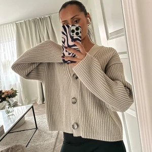 Beige ribbad kofta från H&M - Säljer en superfin beige kofta från H&M i ribbat material. Storlek XS. Den har en v-ringad design med stora knappar framtill. Perfekt för höst och vår när du vill ha något mysigt men ändå stilrent. Passar både till vardags och lite finare tillfällen!