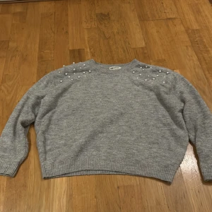 Grå tröja med pärlor från H&M - Säljer en superfin grå tröja från H&M med pärldetaljer på axlarna. Perfekt för både vardag och fest! Tröjan är i bra skick och har långa ärmar, dock har det trillat av nån pärla och visa har tappat färg. Men inget som förstör helhets intrycket. Den är gjord i ett mjukt material som håller dig varm under kyliga dagar.