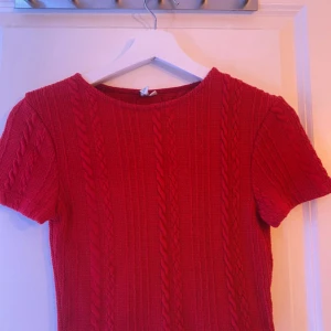 Röd stickad tröja - Säljer en superfin röd stickad tröja med korta ärmar. Perfekt för höst och vår, den har ett snyggt flätmönster som ger en extra touch. Tröjan är i mycket bra skick och passar perfekt för en casual look. Skön och stilren!