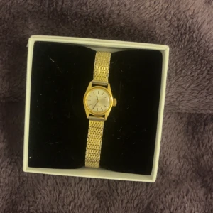 Elegant guldfärgad klocka - Säljer en elegant guldfärgad klocka med ett klassiskt armband i metall. Klockan har en stilren urtavla och kommer i en snygg förpackning. Perfekt för både vardag och fest! ✨