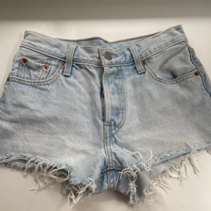 Levis 501 jeans shorts - Levis jeans shorts i bra skick. Ljusblåa med silver och koppar knappar. Beige/ljusgula sömmar. Ganska korta.