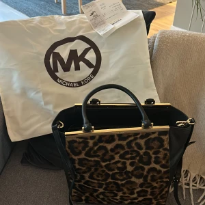 Leopardmönstrad handväska från Michael Kors - Säljer en supercool leopardmönstrad handväska från Michael Kors. Väskan har svarta detaljer och en snygg guldfärgad kant upptill. Perfekt för att ge din outfit en extra touch av stil! 🐆✨ Finns kvitto ej använd, nypris 2260