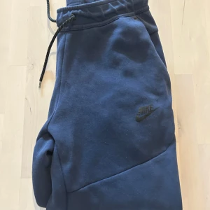 Mörkblå mjukisbyxor från Nike - Säljer nu ett par riktigt snygga Nike tech mjukisbyxor då dom är för små för mig. De är i väldigt bra skick och har inga defekter. Perfekt att köpa nu inför hösten och  vintern. Vid funderingar är det bara att skriva i dm! 