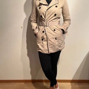 Beige trenchcoat med gulddetaljer, Mango. - Skick: Fint. En trasig knapp och ej original-skärp