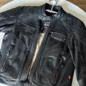Skinnjacka - Säljer en fantastisk skinnjacka från Richa, som är i nyskick och knappt använd. Det eleganta svarta skinnet är av högsta kvalitet och ger jackan en lyxig och tidlös look. Den quiltade axeldesignen tillför både stil och komfort, medan dragkedjedetalje