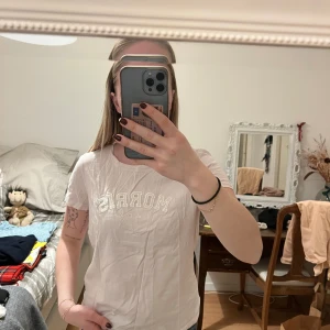 Vit t-shirt från Morris - Säljer en ljus rosa t-shirt från Morris med texttryck på framsidan. T-shirten har en rund halsringning och korta ärmar. Perfekt för en avslappnad stil.