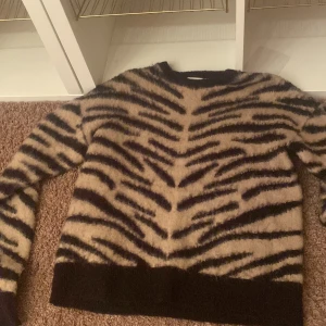 Zebramönstrad tröja i beige och svart - Säljer en trendig zebramönstrad tröja i beige och svart. Tröjan har långa ärmar och en rund halsringning. Perfekt för att ge din outfit en djärv touch!