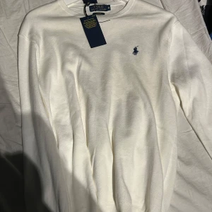 Vit tröja från Ralph Lauren - Säljer en stilren vit tröja från Ralph Lauren i slim fit. Tröjan är tillverkad i mjuk Pima bomull och har en broderad logotyp på bröstet. Perfekt för en klassisk och elegant look. Säljer den för att jag råka köpa fel storlek  och har aldrig använt den förutom när jag provade den. Pris kan diskuteras vid snabb affär 