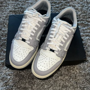 Amiri sneakers  - Amiri grå sneakers är stiliga och exklusiva skor med en modern design. De är tillverkade i högkvalitativa material, som läder och mocka, och har en distinkt, urban känsla. Sneakersen har en sportig men samtidigt lyxig look med detaljer som metalliska inslag, signaturdetaljer och en sula som ger bra komfort. 