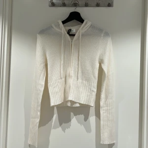 Stickad ziptröja - En stickad tröja med dragkedja i färgen krämvit som slutar ungefär över höfterna. Används endast 1 gång och är i storlek XS från HM. Väldig charmig passform med lång mudd i midja och i längre armar.