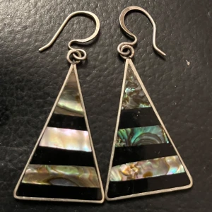 Triangulära örhängen med pärlemor och svart mönster - Unika triangulära örhängen med ett stilrent mönster av pärlemor och svarta ränder. Perfekta för att ge en elegant touch till din stil. Tillverkade i Mexiko.