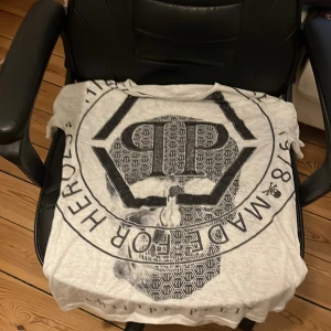 Vit t-shirt från Philipp Plein - Cool vit t-shirt från Philipp Plein med stort tryck av en dödskalle och texten 'Admirable Plein Squad'. T-shirten har korta ärmar och ett unikt mönster med logotypdetaljer. Perfekt för en edgy look!