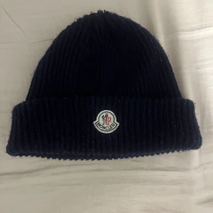 Svart ribbad mössa från Moncler - Snygg marinblå mössa från Moncler. Perfekt för vintern och dess kyliga dagar. Hör av er vid minsta intresse 