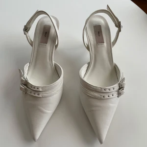 Vita kitten heals med spännen - Vita kitten heals från Nelly med spetsig tå och smal klack. Skorna har dubbla remmar med spännen. Perfekta att både klä ner med jeans eller klä upp till fest. Väldigt bra skick förutom lite avskavt längst fram (se bild 4). Klackhöjd: 4,5 cm! Kan mötas upp i Sthlm, annars står köparen för frakten 💕