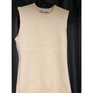 Beige ärmlös klänning från Zara - Snygg beige ärmlös klänning från Zara med en stilren design. Klänningen har en rund halsringning och en figurnära passform som framhäver silhuetten. 