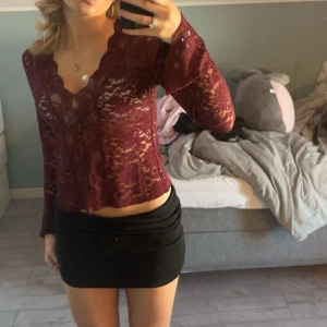 Vinröd spetsblus från Gina - elegant vinröd spetsblus från Gina. Blusen har långa ärmar och en v-ringad design med knappar framtill. Perfekt för en stilfull look. Storlek M men känns mer som s