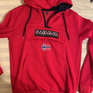 Röd hoodie från Napapijri - Snygg röd hoodie från Napapijri med dragkedja och norsk flagga på framsidan. Perfekt för kyliga dagar med sin bekväma passform och stilrena design.