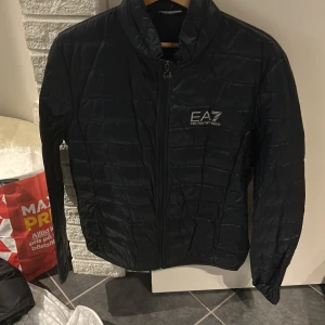 Svart quiltad jacka från EA7 - Snygg svart quiltad jacka från EA7 med dragkedja framtill. Perfekt för kyligare dagar med sin stilrena design och bekväma passform.