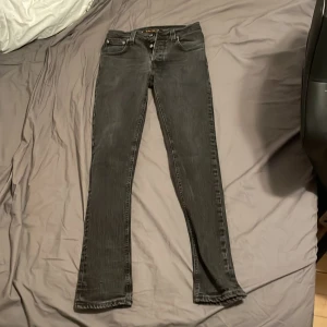 Nudie Jeans Grim Trim - Snygga svarta jeans från Nudie Jeans med en klassisk straight passform. De har en midwaist och är perfekta för en stilren look. Jeansen har fem fickor och stängs med dragkedja och knapp.