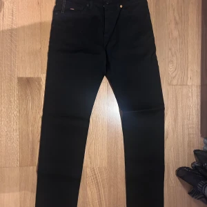 Svarta slim fit jeans från Boss - HELT NYA snygga svarta slim fit jeans från Boss. De har en klassisk design med fem fickor och orangea sömmar som ger en cool kontrast. Perfekta för en stilren look. NYPRIS är 1299. W31 L32. Modellen är 'MAINE.'