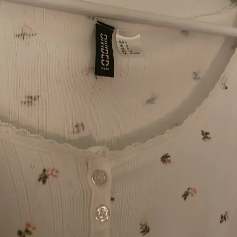 Söt vit topp från h&m med små blommor och knappar framtill. Den har korta ärmar med volangdetaljer och en rund halsringning. Perfekt för en somrig look!. Yläosat.
