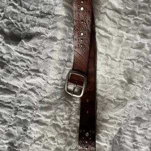 Brunt skärp med nitar - Snyggt brunt skärp med silverfärgad spänne och dekorativa nitar. Saknar några få stenar men de är inget som man tänker på