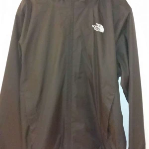 Brun vindjacka från The North Face - Säljer en brun vindjacka från The North Face med dragkedja och huva. Perfekt för blåsiga dagar och har en stilren design med logotyp på bröstet. Köpt från Zalando 