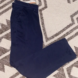 Mörkblå kostymbyxor - Snygga mörkblå kostymbyxor med en klassisk straight passform. Perfekta för en stilren look. Byxorna har knappar bak och är tillverkade i ett elegant material.