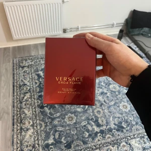 Versace Eros Flame Eau de Parfum - Säljer en elegant (och oöppnad) Versace Eros Flame Eau de Parfum i en lyxig röd förpackning. Flaskan innehåller 200 ml av denna intensiva och maskulina doft, perfekt för den självsäkra mannen. Förpackningen har en stilren design med guldtext och Versaces ikoniska logotyp.