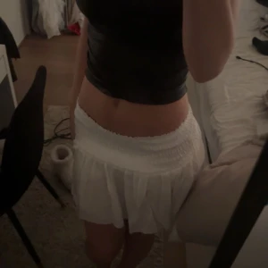 Vit kortkjol med volang - Säljer en söt vit kortkjol med volangdetaljer. Kjolen har en elastisk midja för en bekväm passform och är perfekt för varma dagar. Den här samt short under som ej syns igenom!