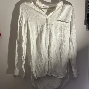 Vit långärmad skjorta - Säljer en stilren vit långärmad skjorta med klassisk krage och bröstficka. Perfekt för en elegant och avslappnad look. Skjortan har en normal passform och är tillverkad i ett lätt och bekvämt material.