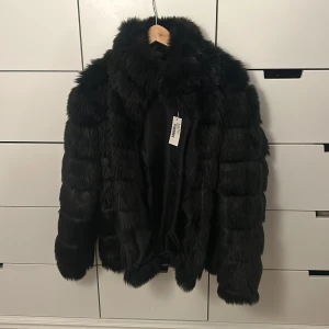 Svart pälsjacka från Nelly - Säljer en svart puffer pälsjacka från Nelly. Jackan har en fluffig design med långa ärmar och en mysig krage. Perfekt för att hålla sig varm och stilren under kyliga dagar. Lappen är kvar! 