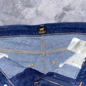 Mörkblå jeans från Lee - Snygga mörkblå jeans från Lee i modellen Elly. De har en klassisk femficksdesign med guldfärgade sömmar och en knappgylf. Perfekta för en stilren look.