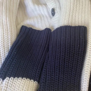 Vit och marinblå stickad kofta från Race Marine - Säljer en snygg vit och marinblå stickad kofta från Race Marine. Koftan har knappar framtill och en broderad logga på ärmen. Perfekt för kyliga dagar med sin mysiga och stilrena design.står ej för frakt