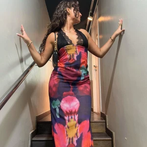 Färgglad långklänning med spetsdetaljer - Snygg långklänning med ett färgglatt mönster i rött, rosa, gult och grönt. Klänningen har svarta spetsdetaljer vid bysten och är ärmlös. Perfekt för en somrig look!