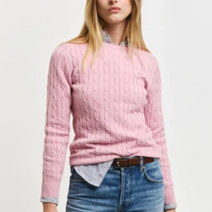 Tröja från GANT - Säljer en söt rosa stickad tröja från GANT. Tröjan har ett klassiskt kabelstickat mönster och långa ärmar. Perfekt för en stilren och bekväm look.