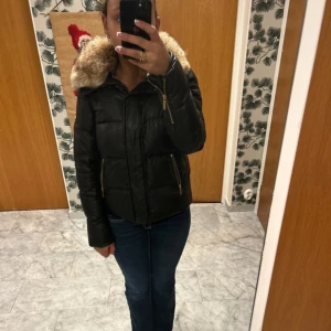 Svart dunjacka från Michael Kors - Snygg svart dunjacka från Michael Kors med äkta coyote-päls på huvan. Jackan har dragkedja och långa ärmar, perfekt för kalla vinterdagar. Säljer pga att den inte kommer till användning. 💞