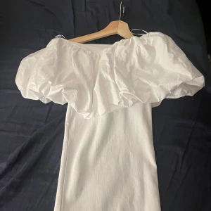 Vit offshoulder klänning - Elegant vit offshoulder klänning med volangdetaljer. Perfekt för sommarens festligheter.