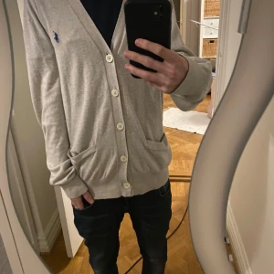 Beige kofta från Polo Ralph Lauren - Säljer en stilren beige kofta från Polo Ralph Lauren med knappar framtill och två fickor. Den har ett broderat blått logotypmärke på bröstet. Perfekt för en avslappnad och elegant look. Köpt här på plick men säljer den pågrund av att den var för stor på mig som är 170 lång och väger 52  skick: 9/10