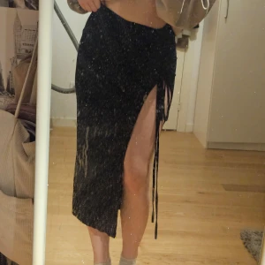 Svart långkjol med slits - Trendig svart långkjol med hög slits och snörningsdetalj på sidan. Kjolen har en åtsittande passform och är perfekt för en stilren look.