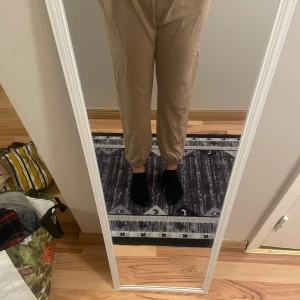 Beige/bruna byxor - Säljer ett par bekväma beige byxor med elastisk midja och avsmalnande ben. Perfekta för en avslappnad stil.
