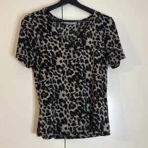 Leopardmönstrad topp från ChaCha - Snygg leopardmönstrad topp från ChaCha i svart och beige. Toppen har korta ärmar och en normal passform, perfekt för att ge en trendig touch till din outfit. Den har teckna på användning men är fortfarande super fin💗