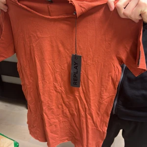 Orange t-shirt från Replay - Säljer en snygg orange t-shirt från Replay. Den har en enkel design med korta ärmar och är perfekt för en avslappnad stil. Märkets etikett sitter kvar, vilket ger en extra touch av stil.
