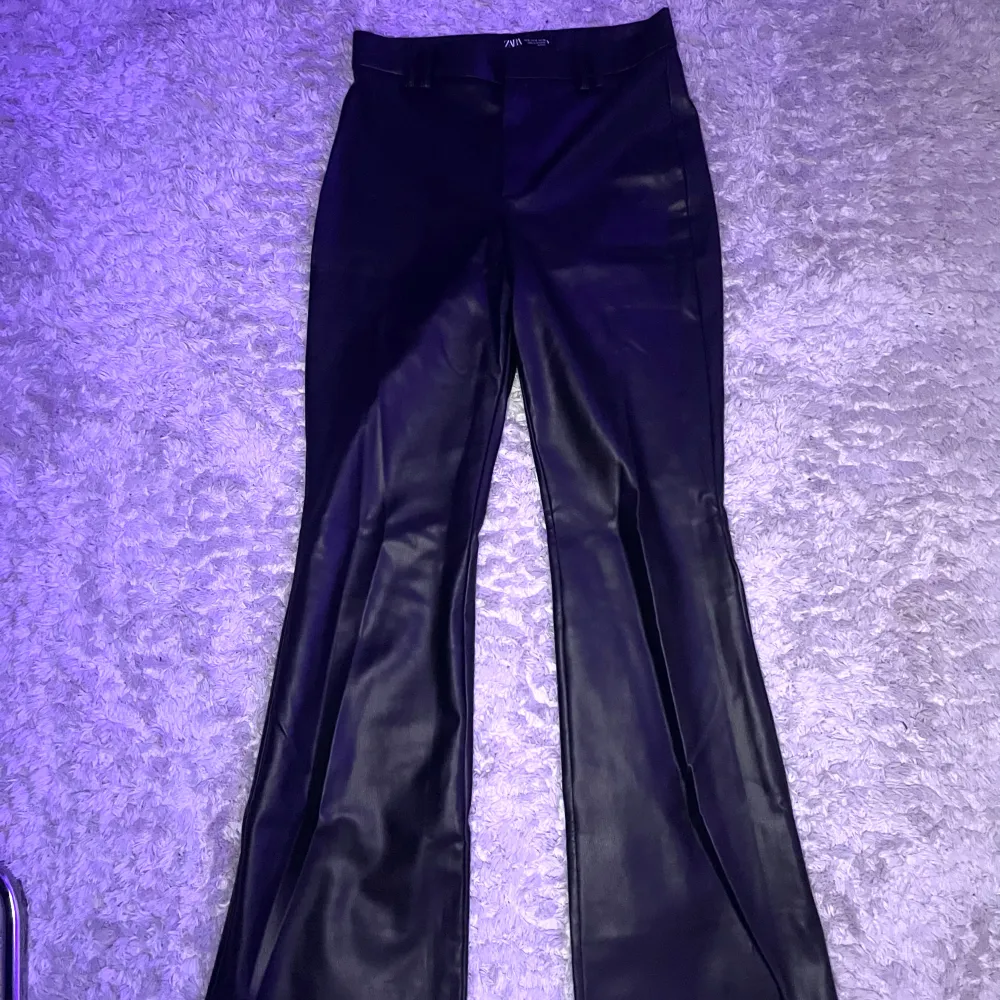 Snygga svarta skinnbyxor med bootcut-stil från Zara. Byxorna har en slät yta och är gjorda i ett skinnmaterial som ger en cool känsla. De är långa så blivit lite slitna längst ner men inget som syns.. Farkut & Housut.